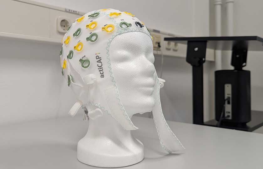 White mannequin head wearing an actiCAP EEG cap with yellow and green sensors in a lab setting.