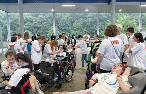 Group of people, including several in wheelchairs, at a covered outdoor event helping and socializing.
