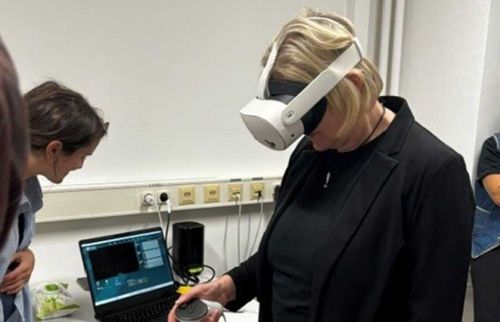 Person wearing a white VR headset while a laptop sits on a lab counter and another person looks on.