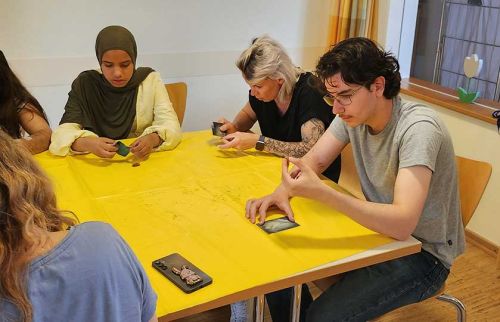 Diverse group of adults seated around a bright yellow table, folding or handling cards during a workshop.