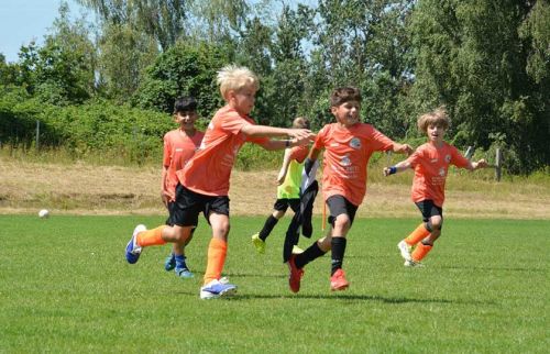 Group of young boys in orange jerseys sprint across a sunny soccer field with a ball nearby.] ,Oops
