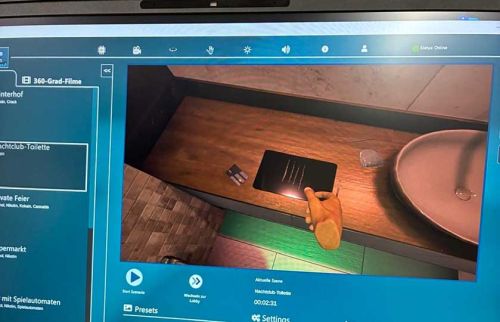 Software interface on a monitor showing a 3D room scene: a hand holds a black card over a wooden counter beside a sink.