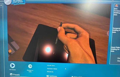 Close-up of a hand holding a stylus and touching a tablet screen during a demonstration.